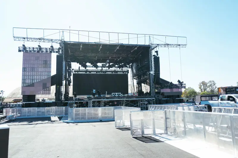 A festival stage part-built in daylight: truss up, screens hung, barricade going in, crew on deck.